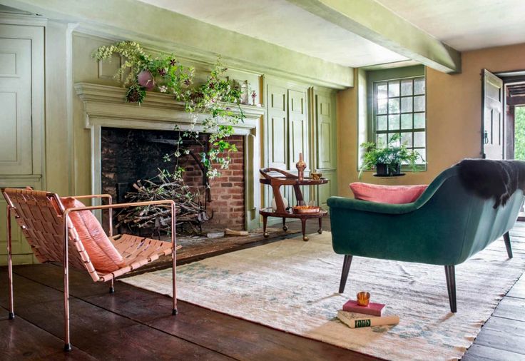 A teal chair with a pink cushion facing a fireplace in a green paneled room.