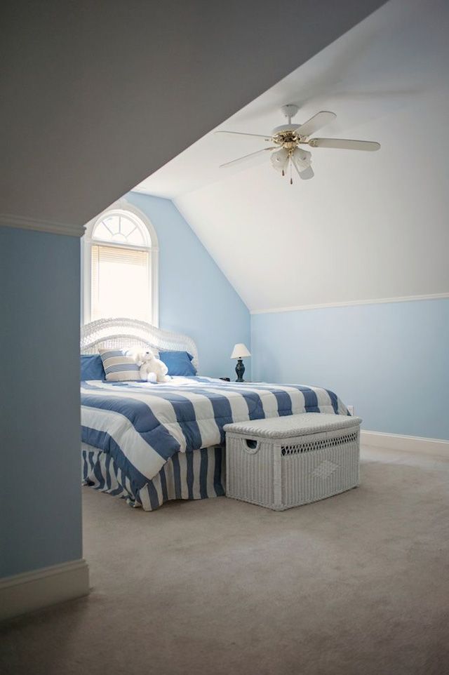 A pale blue attic bedroom with broad striped bedding and a white chest at the foot of the bed.