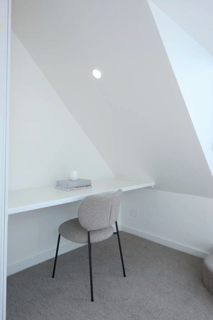 A long white desk and gray chair beneath a sloping ceiling.