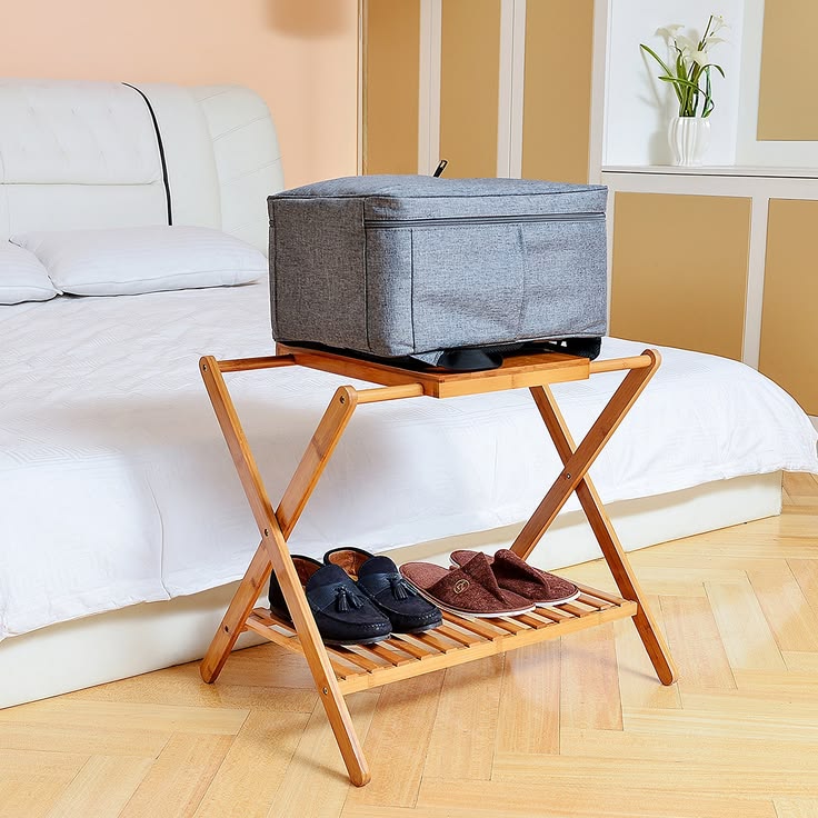 A gray case on a folding luggage rack with shoes on the lower shelf beside a bed.