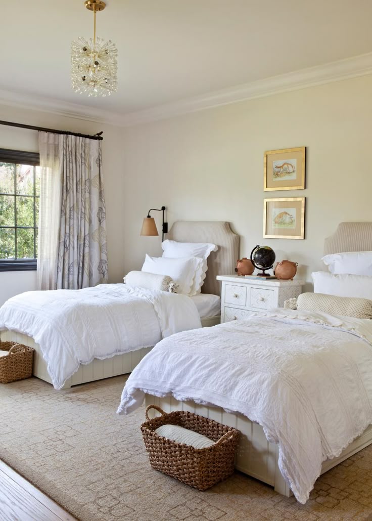Two beds with white bedding, baskets at their feet, and a white chest between them.