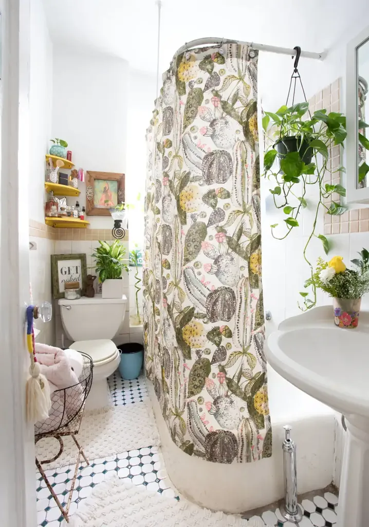 A botanical print shower curtain hangs beside a white pedestal sink in a bathroom with small black and white floor tiles.