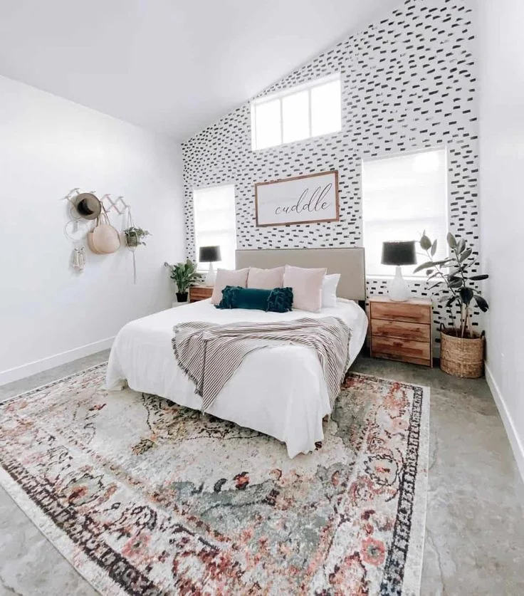 A black-and-white patterned wall rises behind a pale bed between two windows under a sloping ceiling.