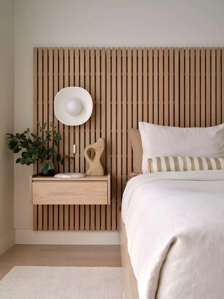 A low vertical slat panel continues behind a bed and floating bedside drawer beneath a pale wall.