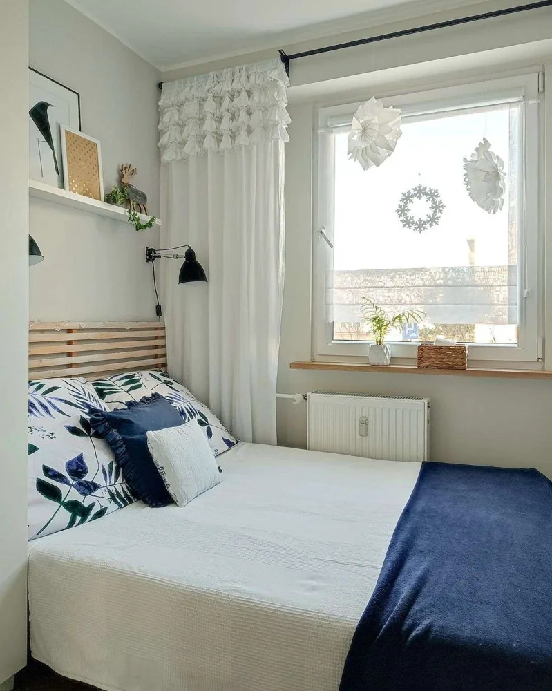 A black wall light sits above blue-and-white bedding beside a window.