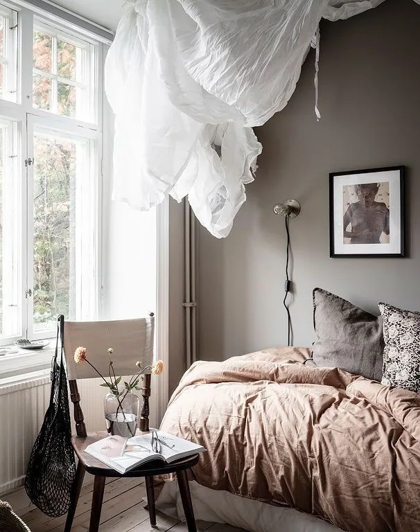 Gray bedroom walls frame a bed with dusty pink bedding and dark gray pillows beside a window.