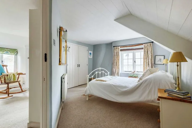 Pale blue walls surround white bedding, cream curtains and yellow bedside lamps.