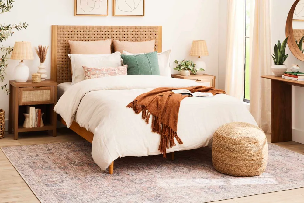 A pale patterned rug extends from under a wooden bed with white bedding and rust accents.