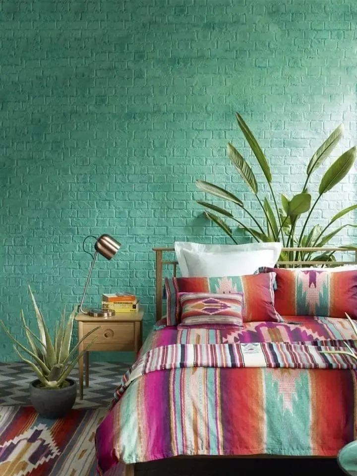 Multicolored striped bedding sits against a teal brick wall beside large plants.