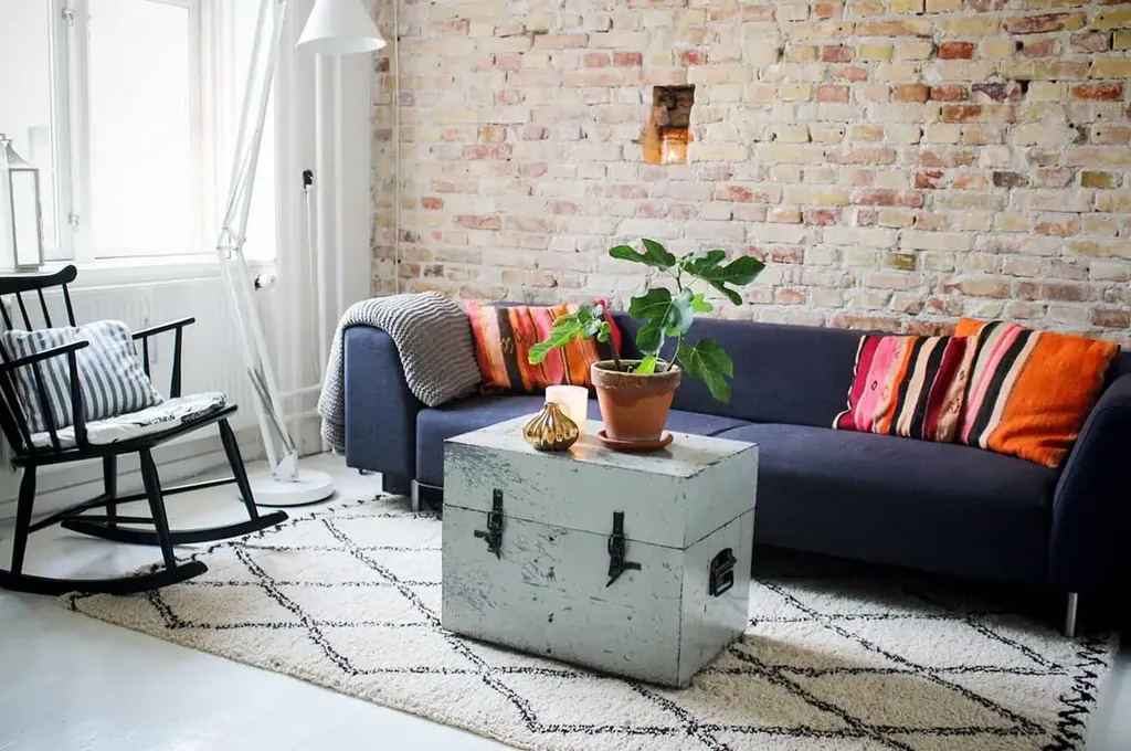 Dark sofa with striped orange pillows, a pale chest coffee table and a cream rug