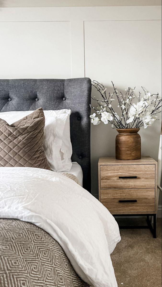 Charcoal buttoned headboard behind white bedding, with a brown quilted pillow, geometric throw, and wood-toned nightstand.