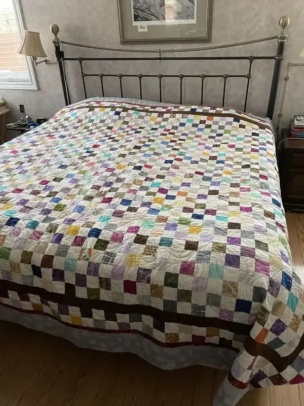 A colorful patchwork quilt covers a bed with a dark metal headboard.
