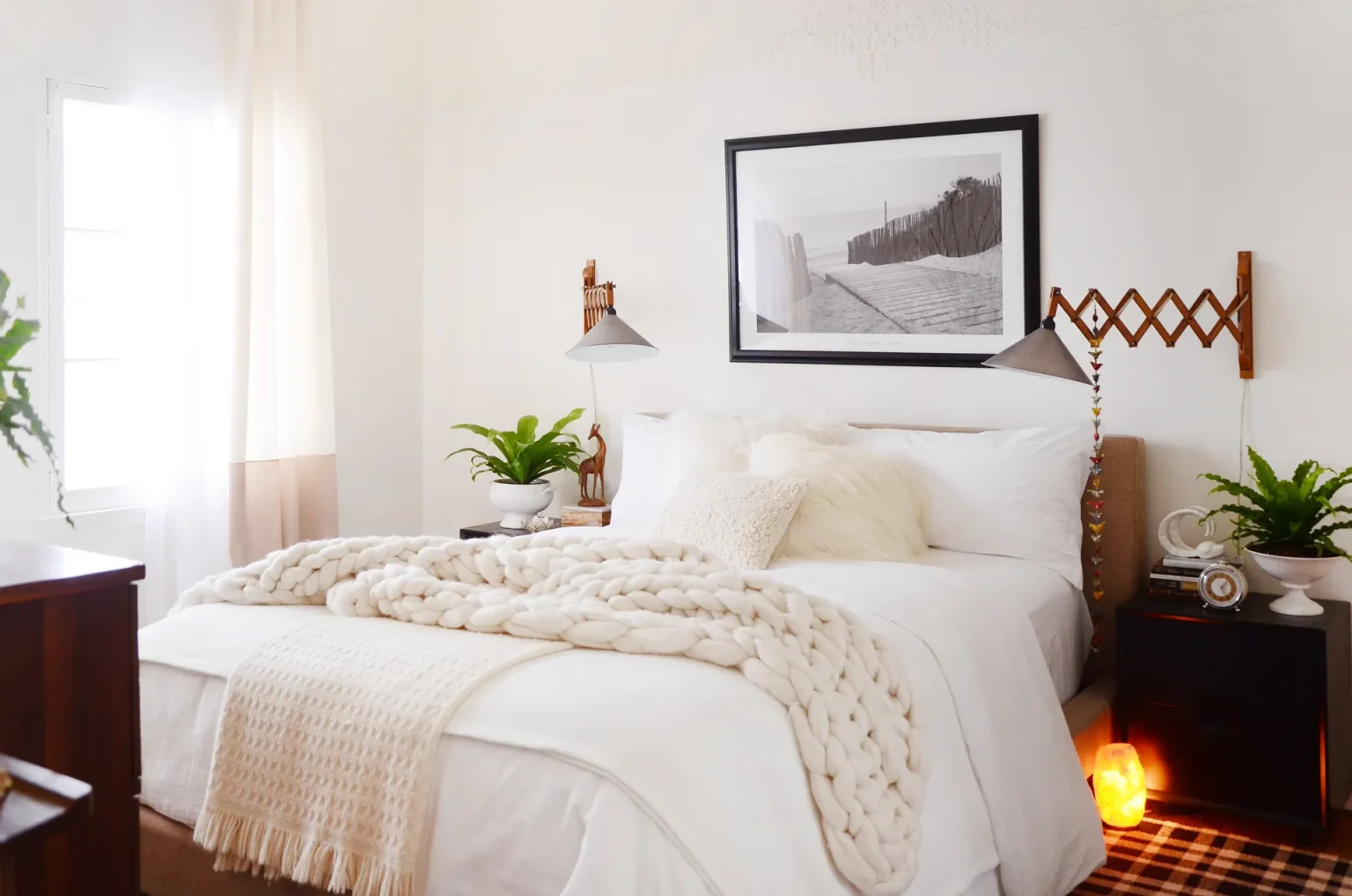 A white bed has a chunky cream throw, wall lamps, and a small amber light near the floor.