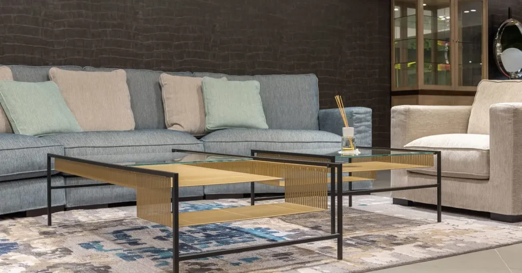 A gray sofa with pale cushions beside a cream armchair and gold-toned glass coffee tables.