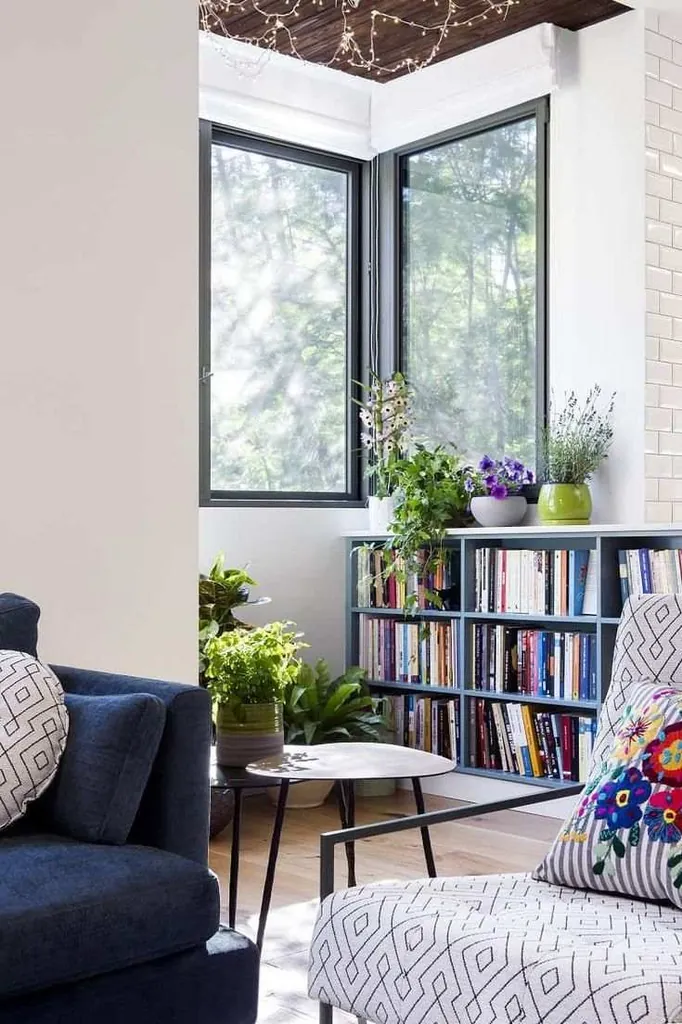 A navy sofa and patterned armchair sit beside a low bookcase and tall corner windows.