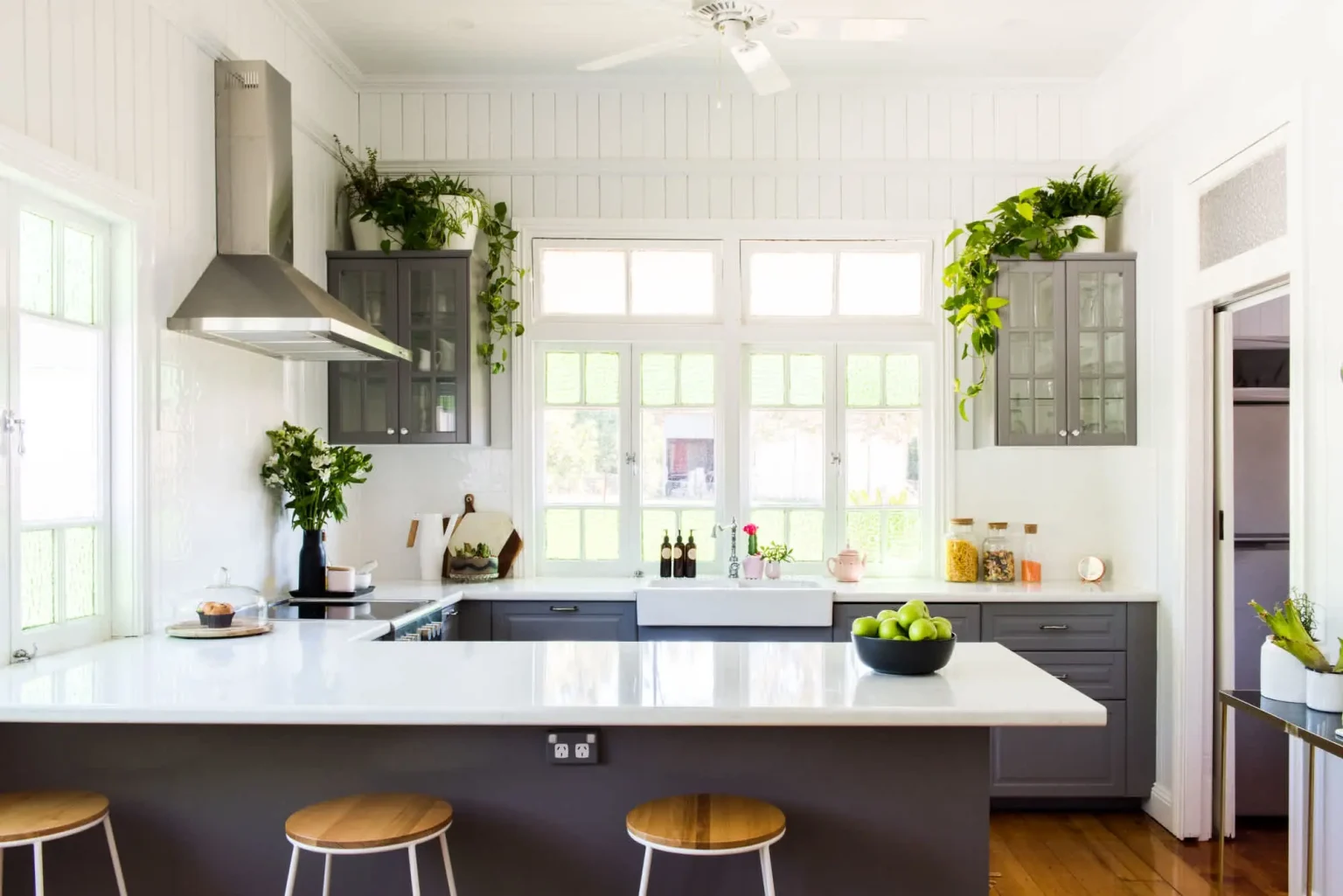 A black bowl of green apples sits on a mostly open white kitchen island.