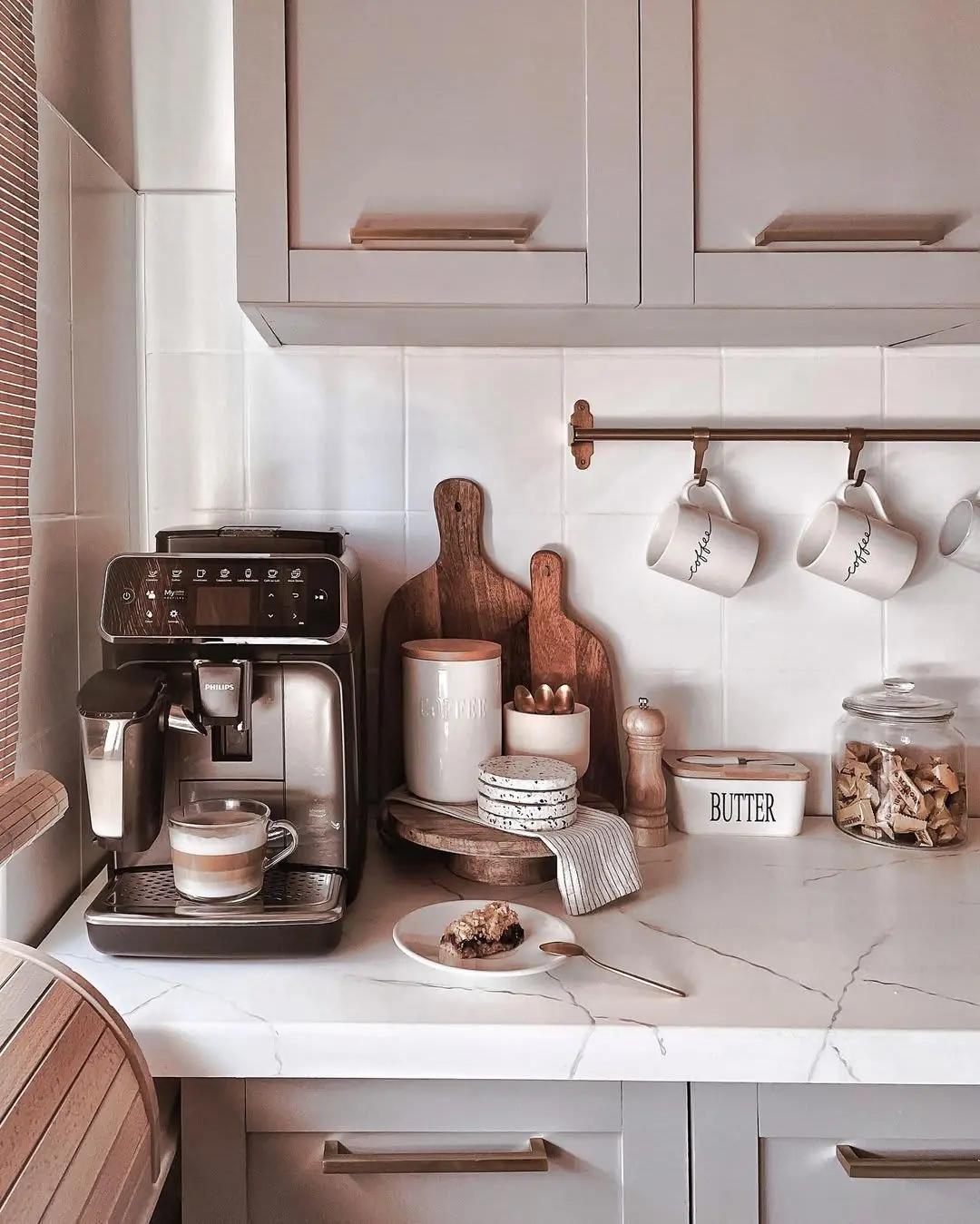 A coffee machine, white canisters, and hanging mugs form a compact counter setup.