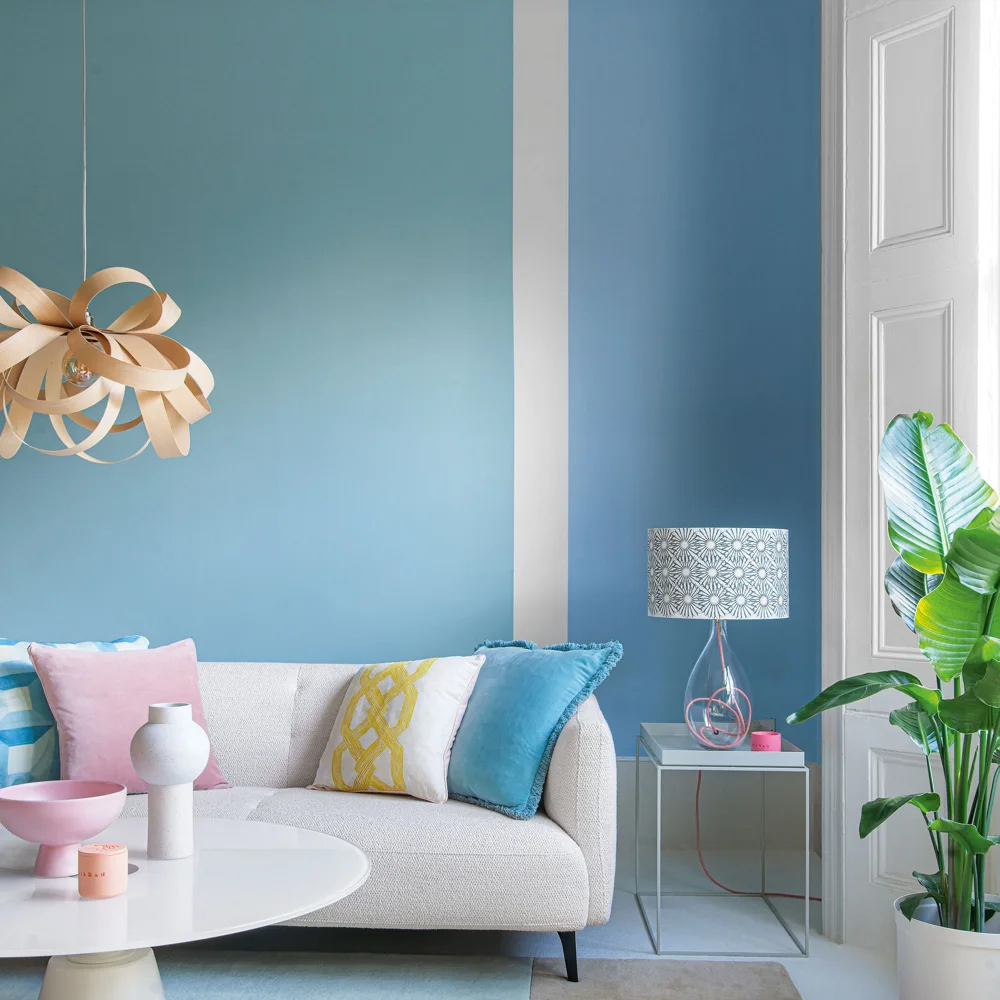 A pale blue wall frames a white sofa with pink, blue and yellow cushions.