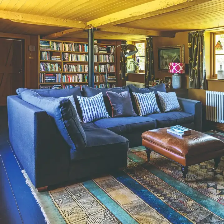 Yellow walls and ceiling frame a blue sectional sofa, brown ottoman and multicolored patterned rug.