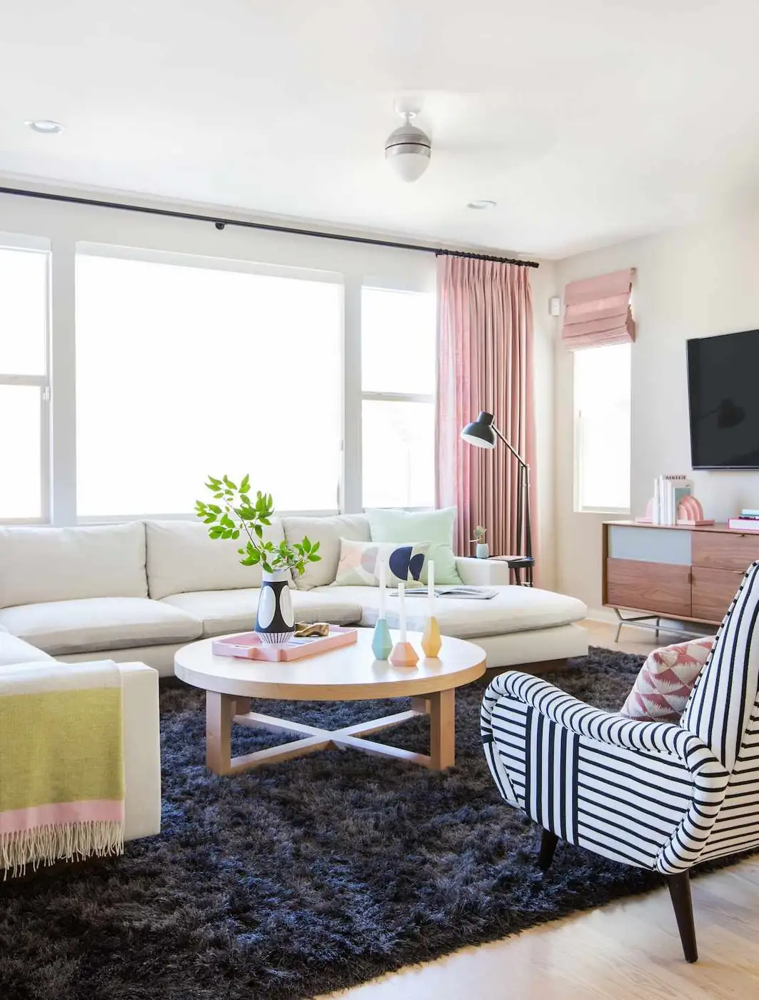 Pink floor-length curtains and a matching folded shade frame a bright living room.