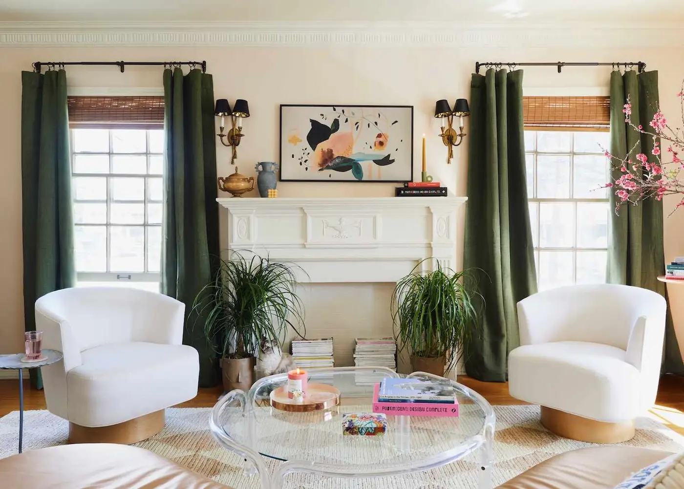 Olive green curtains and brown woven shades flank a white fireplace and white chairs.