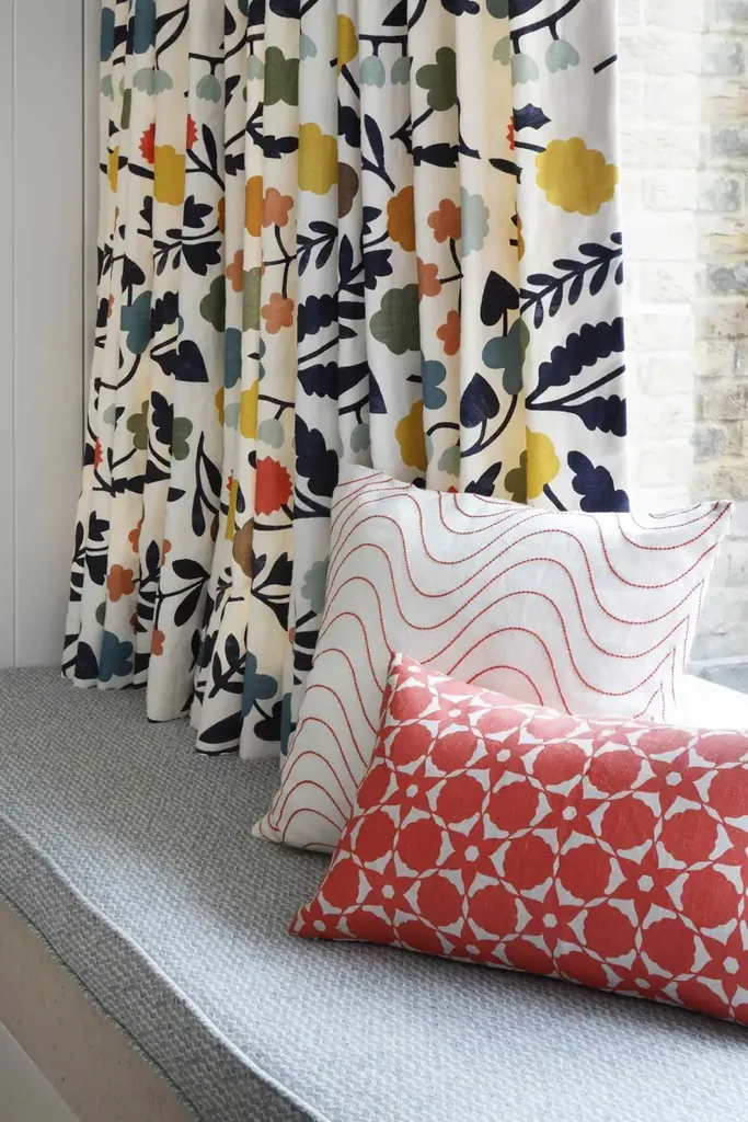 Multicolored floral curtains hang beside a window seat with red and white patterned cushions.
