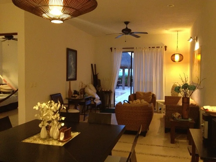 Glowing pendant and wall lights appear across an evening living and dining space with woven chairs.