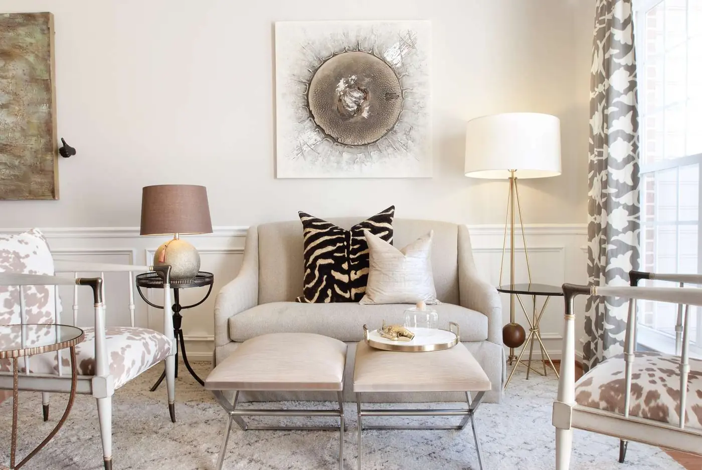 A small table lamp and a tall floor lamp flank pale chairs and matching footstools.