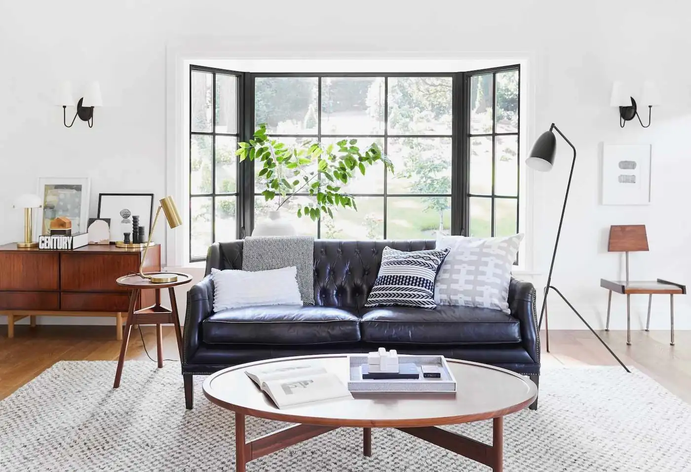 A black angled floor lamp and a brass-colored table lamp flank a black sofa.