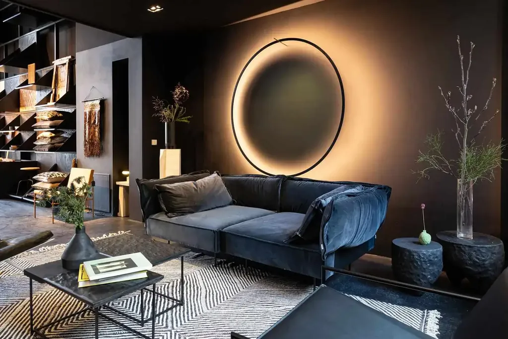 A glowing circular wall fixture behind a blue sofa in a dark interior.
