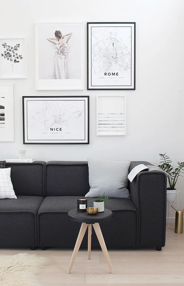 Black and white framed prints hang over a charcoal sofa with pale cushions.