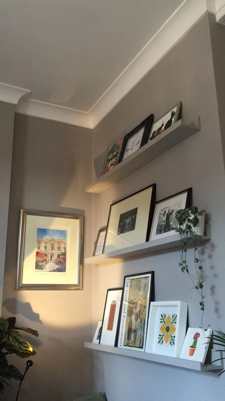 Three slim picture ledges display overlapping framed art beside a doorway.