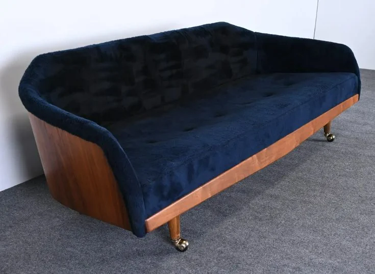 A dark blue sofa has a curved wooden outer shell and small metal feet.