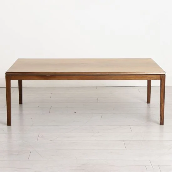 A plain rectangular wooden coffee table stands on four slim legs.