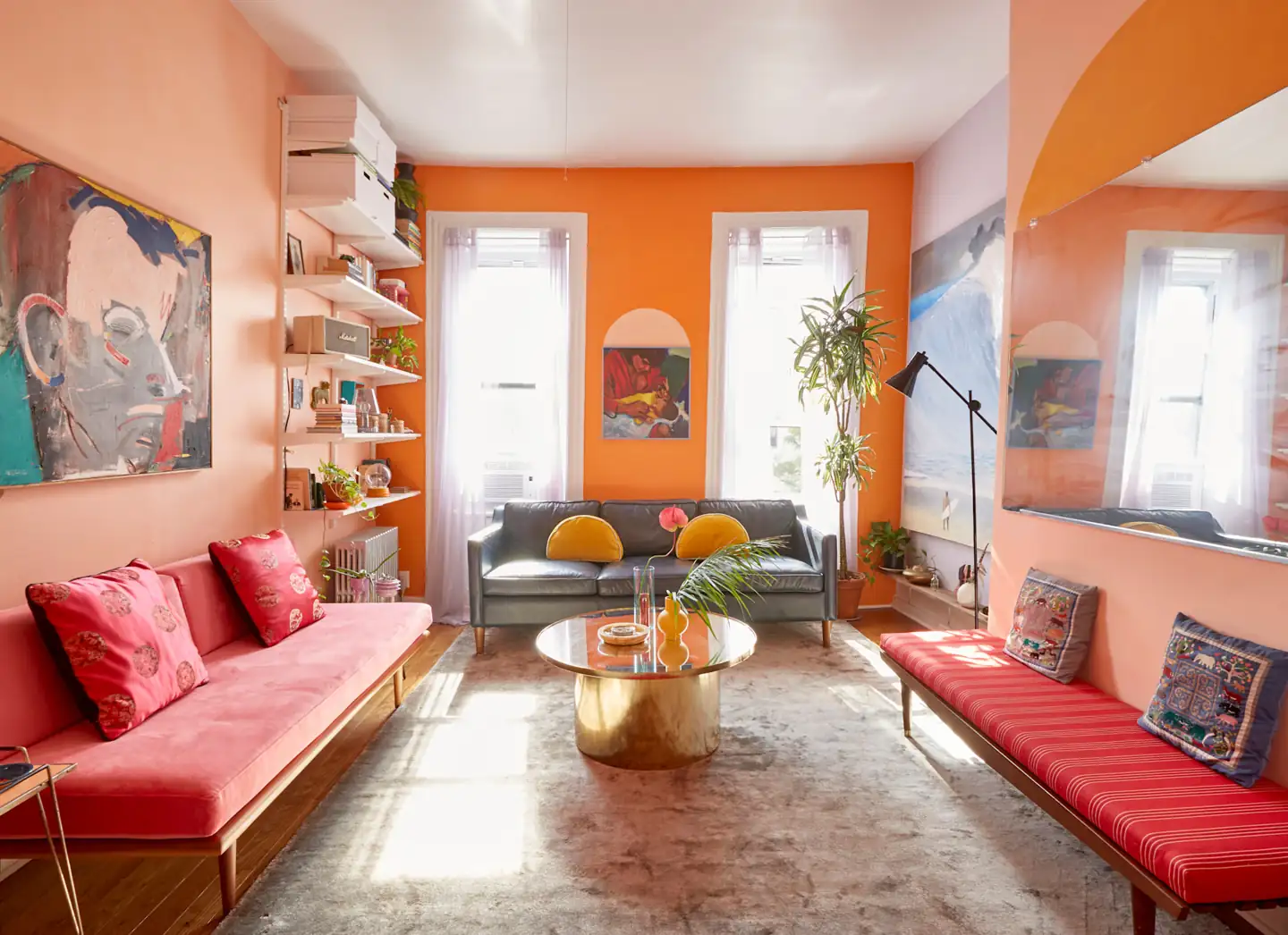 A pink sofa and red bench face each other with a gray loveseat at the window end.