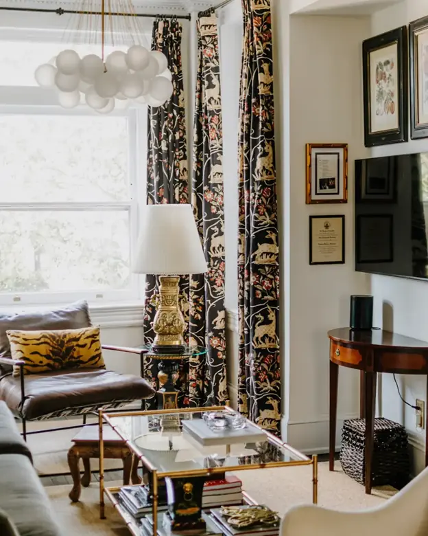 A leather chair sits by a window beside a glass coffee table and a wall-mounted TV.