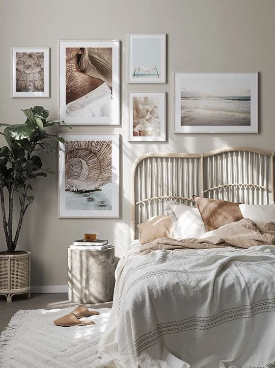 Pale framed pictures hang above a curved woven-looking headboard with tan pillows and a gray striped cover.