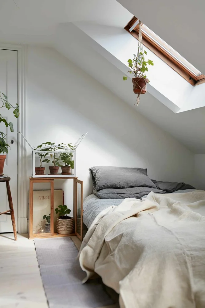 A bed sits under a sloping ceiling beside a skylight and a small table.