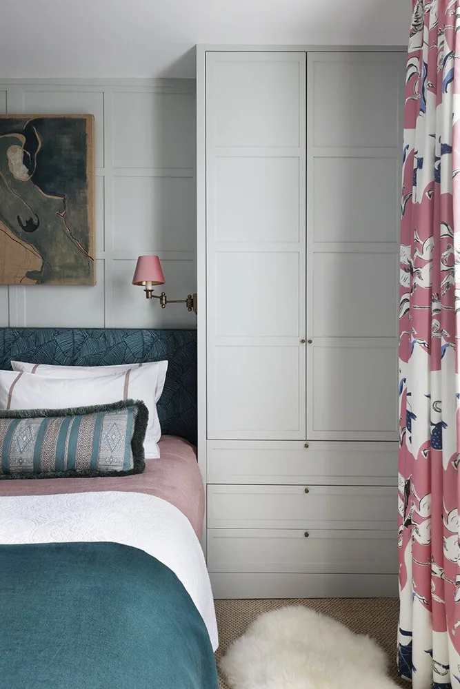 A tall white wardrobe stands beside a bed and a curtain.