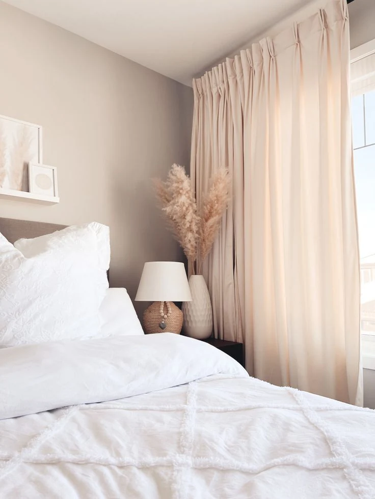 Pale pink curtains beside white bedding and a small bedside lamp.