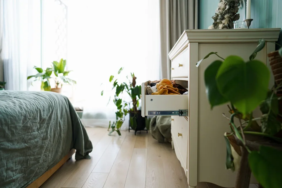 An open drawer in a green bedroom dresser holds clothing.