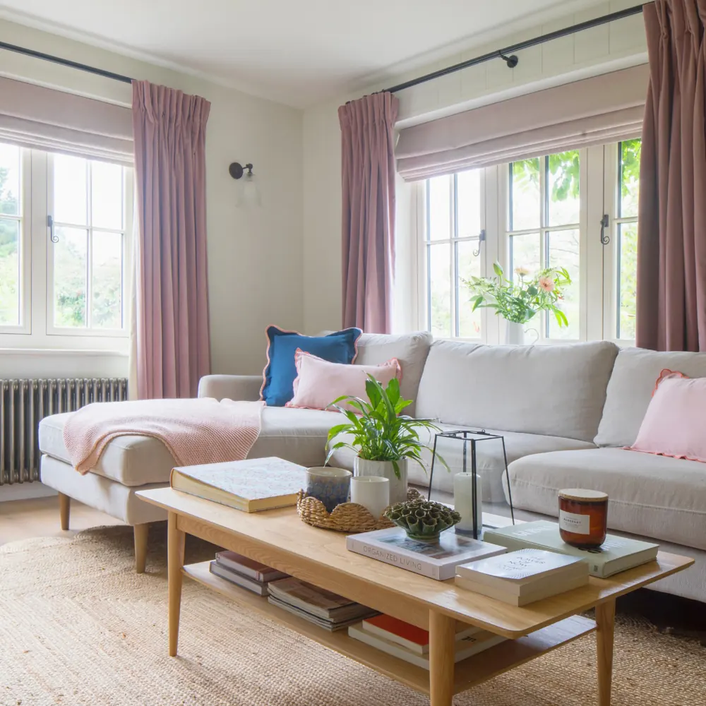 A pale chaise sofa sits beneath a window beside a second window and a low rectangular table.