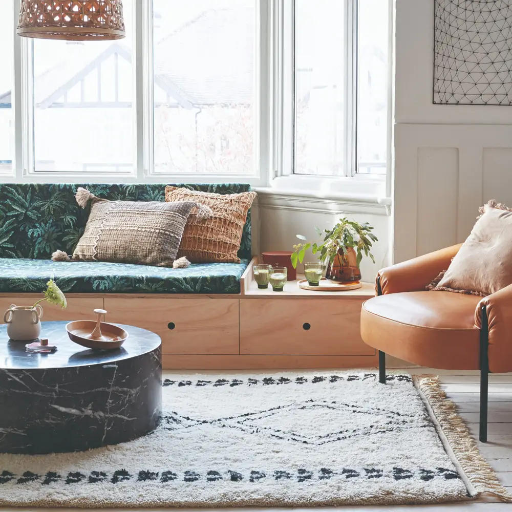 A cushioned seat runs beneath a bay window opposite a separate brown chair and round table.