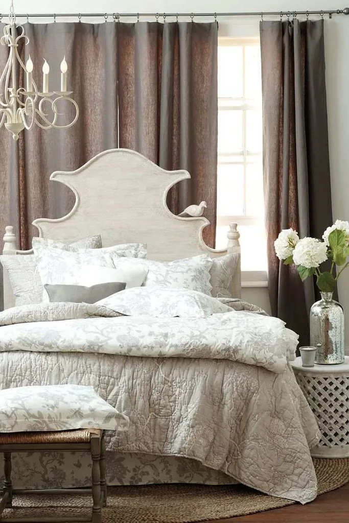 Taupe curtains behind a pale curved headboard and white bedding with gray botanical patterns.