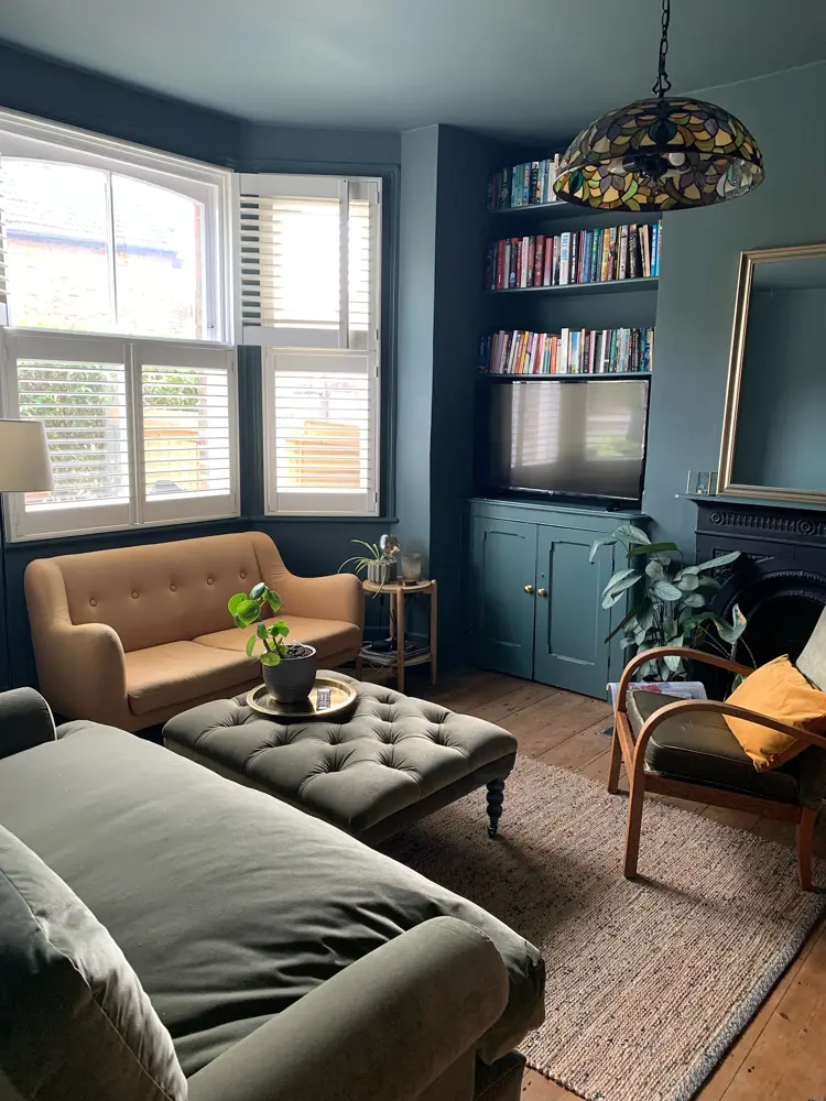 A blue living room has tall bookshelves, a mirror above the fireplace and a tan loveseat.